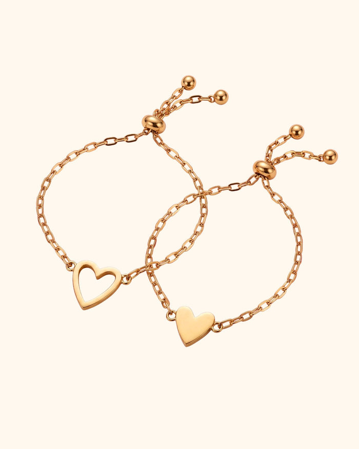 Two gold mother-daughter heart bracelets: an open heart for mom and a filled heart for her daughter, each with an adjustable slider and two small beads
