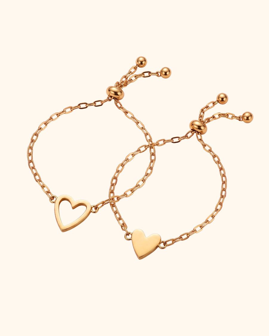 Two gold mother-daughter heart bracelets: an open heart for mom and a filled heart for her daughter, each with an adjustable slider and two small beads