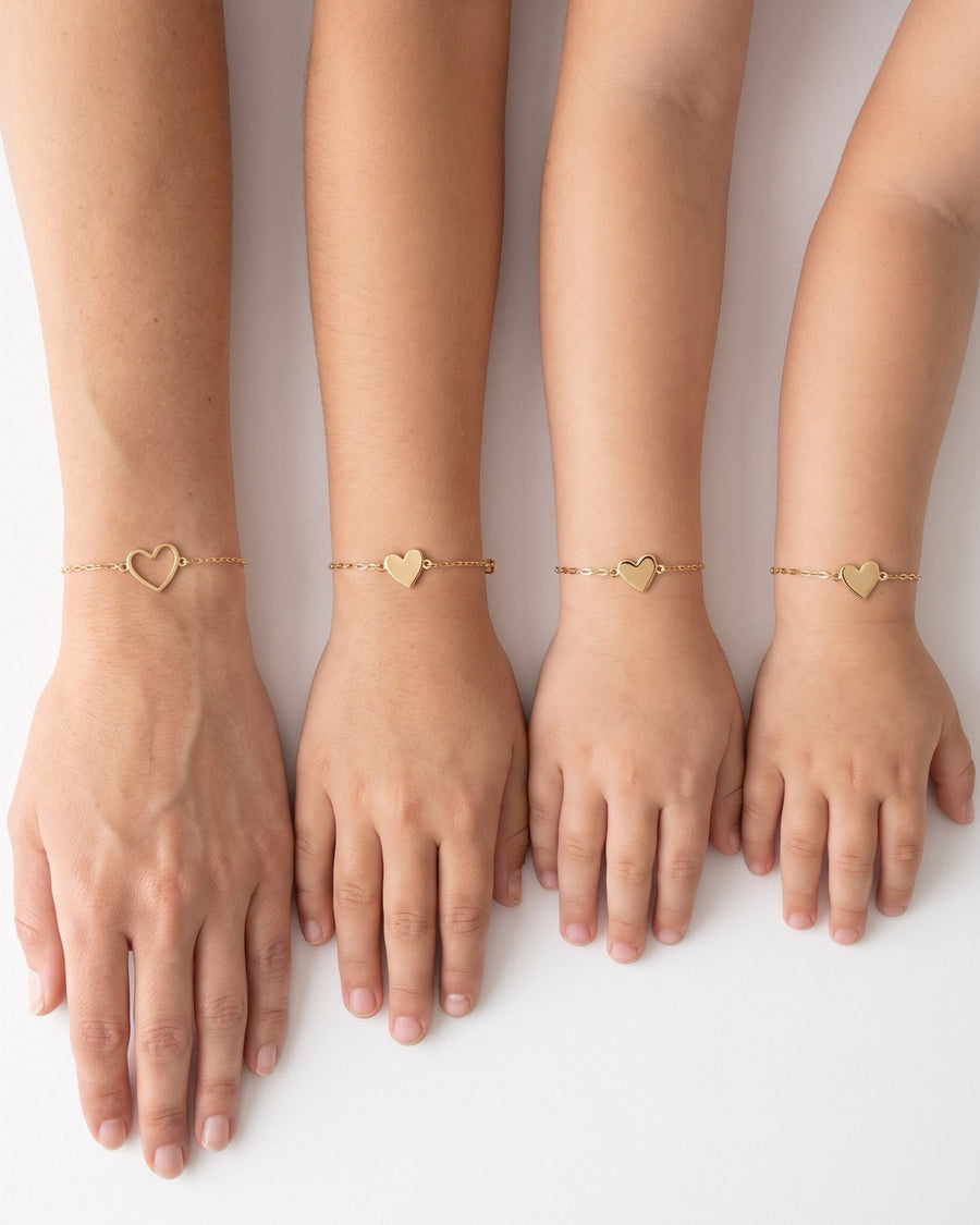 A mother and her three daughters with their arms side by side: open heart bracelet on the mother, a filled heart bracelet on each daughter