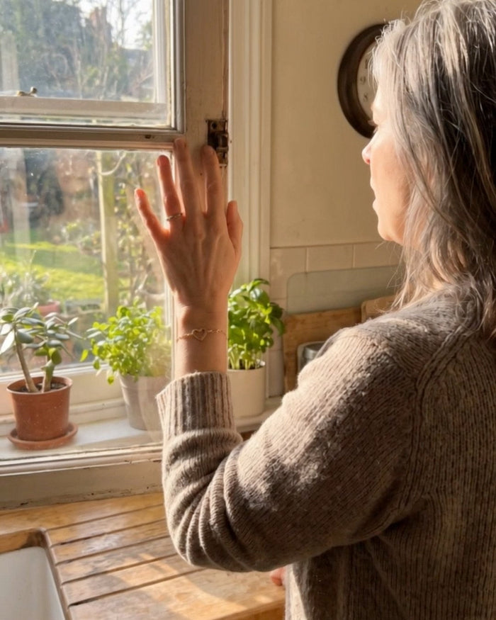 A mother looking out of her kitchen window, wearing her open heart bracelet