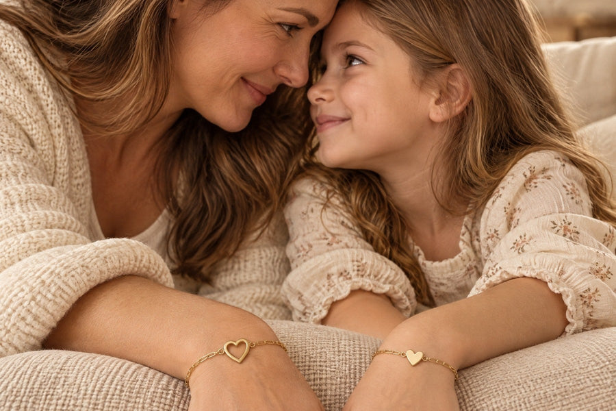 Mother and daughter resting their heads together, the mother wearing the open heart bracelet and the daughter the filled heart bracelet
