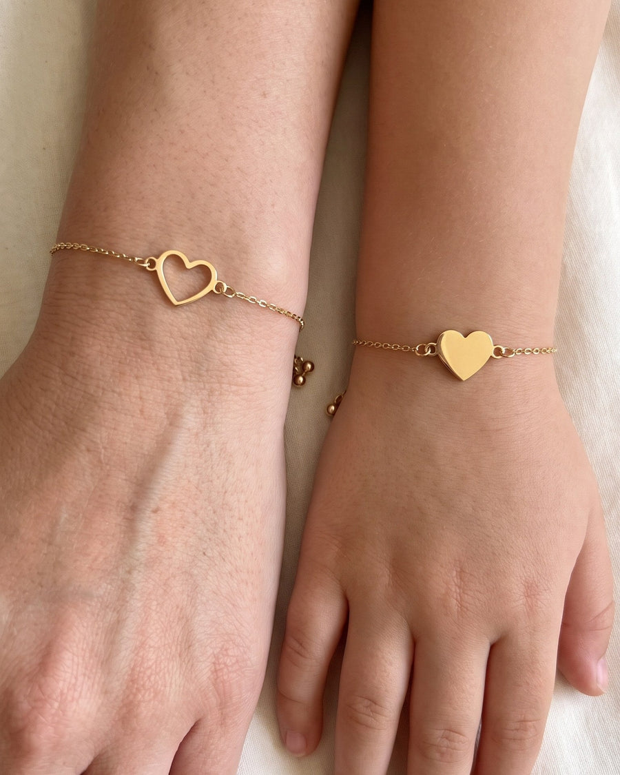 Mother and daughter wrists side by side: gold open heart bracelet on the mother, filled heart bracelet on the daughter